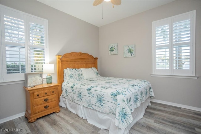 bedroom with multiple windows, wood finished floors, and baseboards