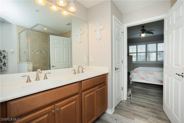 ensuite bathroom with double vanity, a sink, a tile shower, and wood finished floors