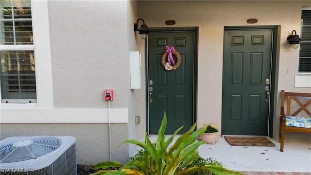 view of exterior entry featuring central air condition unit and stucco siding