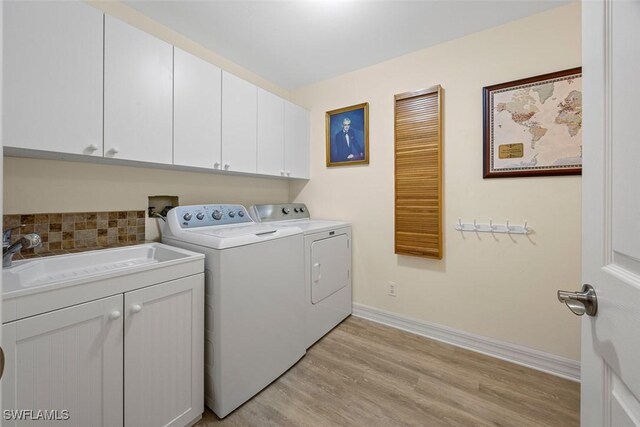 washroom featuring a sink, cabinet space, light wood-style floors, separate washer and dryer, and baseboards