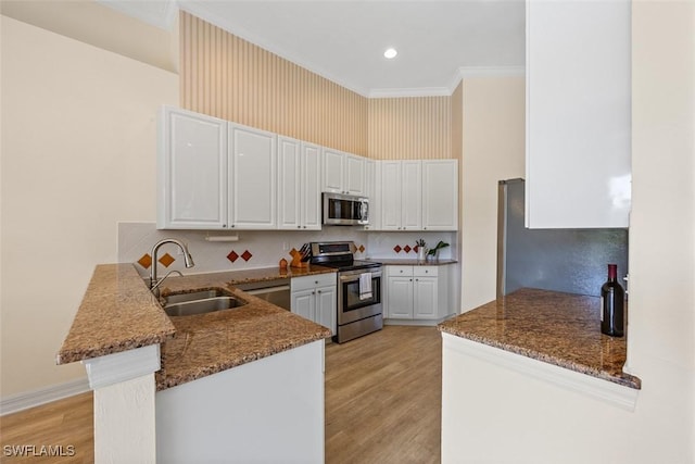 kitchen featuring dark stone countertops, a peninsula, a sink, stainless steel appliances, and white cabinets