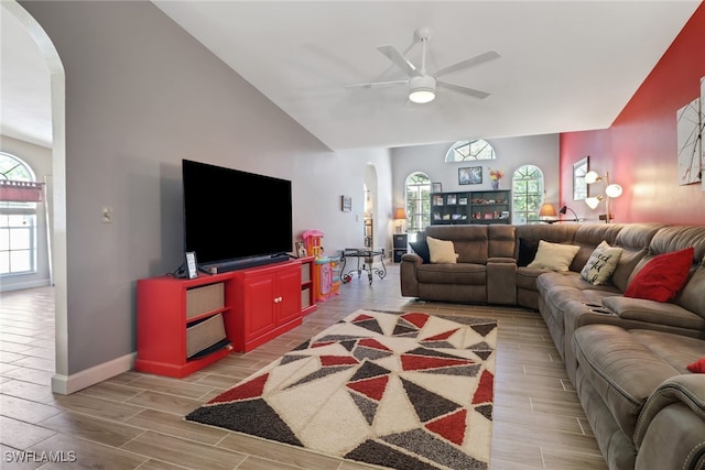 living area with arched walkways, wood finish floors, lofted ceiling, a ceiling fan, and baseboards