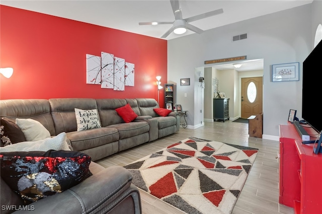 living area featuring ceiling fan, an accent wall, wood finished floors, visible vents, and baseboards