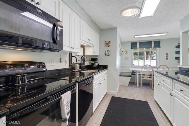 kitchen with wood finish floors, dark countertops, white cabinets, a sink, and black appliances