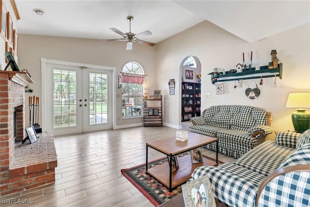 living area featuring lofted ceiling, a fireplace, wood finished floors, a ceiling fan, and french doors