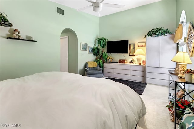 carpeted bedroom with a ceiling fan, arched walkways, and visible vents