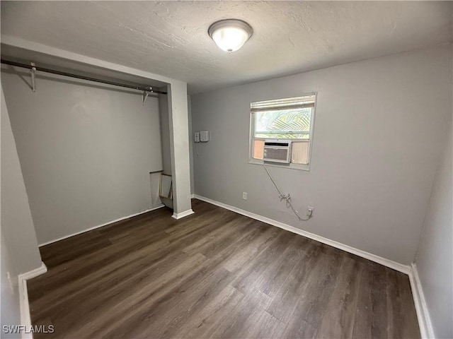 unfurnished bedroom featuring a closet, cooling unit, a textured ceiling, baseboards, and dark wood-type flooring