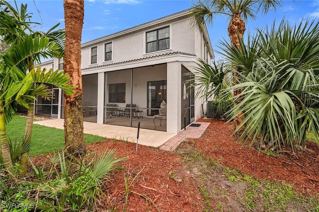 rear view of property featuring a sunroom, a lawn, a patio, and stucco siding