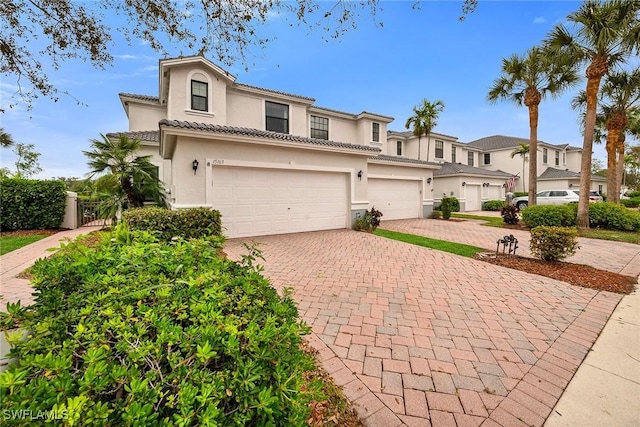 view of front of house featuring a tile roof, a residential view, an attached garage, decorative driveway, and stucco siding