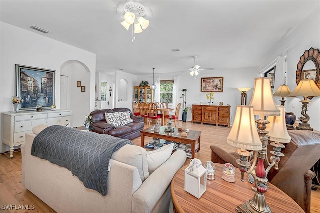 living area with light wood finished floors, visible vents, arched walkways, and a ceiling fan