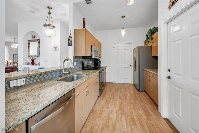 kitchen with light wood finished floors, decorative backsplash, light stone countertops, stainless steel appliances, and a sink