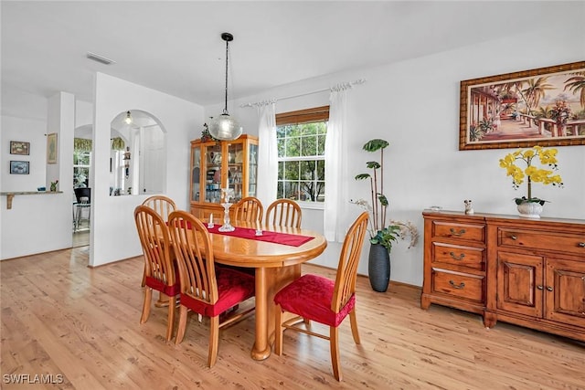 dining space featuring arched walkways, light wood finished floors, and visible vents