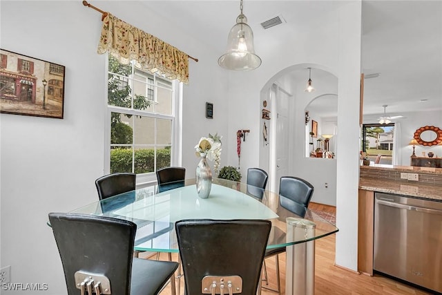 dining space featuring arched walkways, light wood finished floors, visible vents, and a ceiling fan