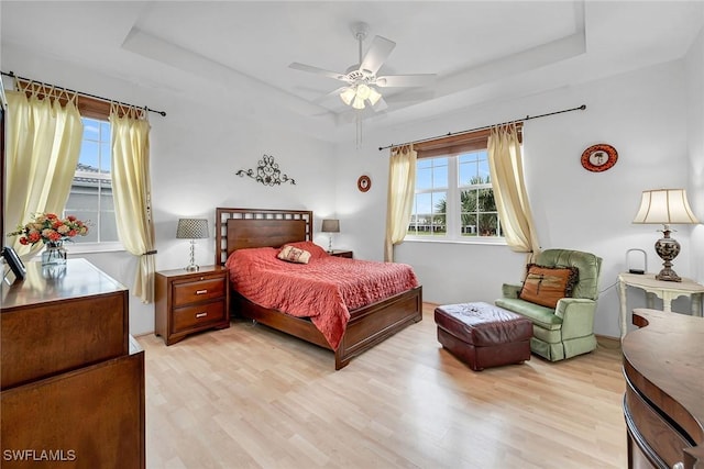 bedroom with light wood-style floors, ceiling fan, and a tray ceiling