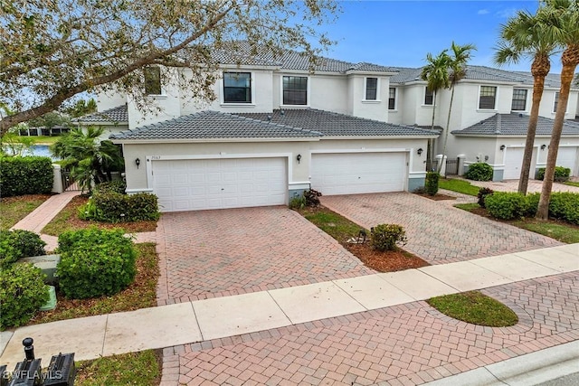 view of front of house featuring decorative driveway, a tiled roof, an attached garage, and stucco siding