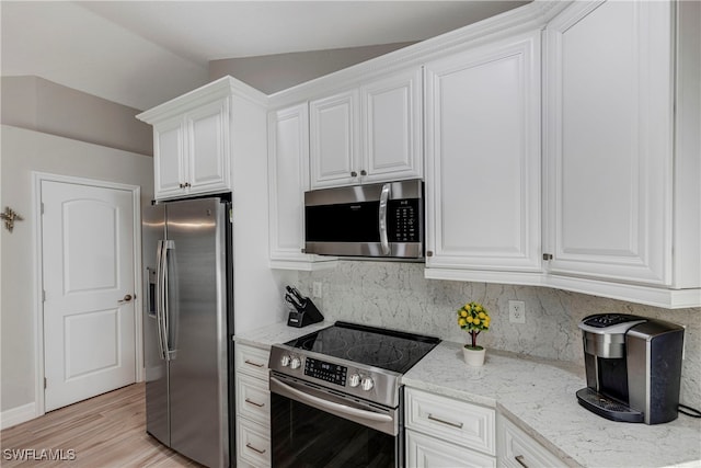 kitchen with light wood finished floors, light stone countertops, stainless steel appliances, white cabinetry, and backsplash