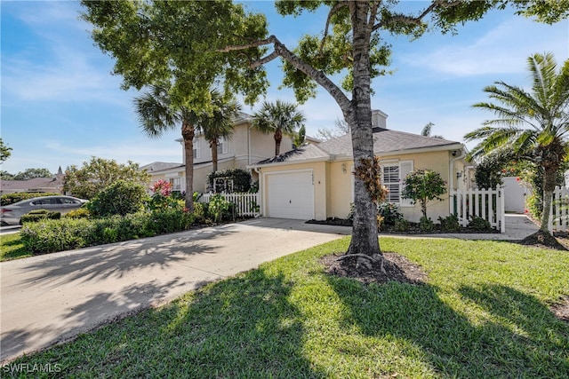 view of front of house with stucco siding, a front yard, fence, a garage, and driveway