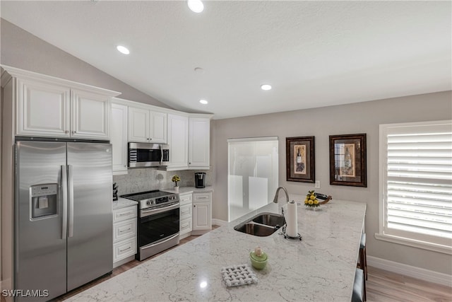 kitchen with light stone counters, appliances with stainless steel finishes, white cabinetry, vaulted ceiling, and a sink