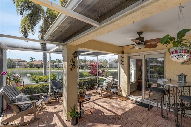 view of patio featuring a water view, glass enclosure, and ceiling fan