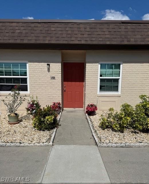 property entrance featuring mansard roof, a shingled roof, and brick siding