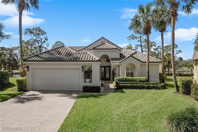 mediterranean / spanish home featuring a garage, a tiled roof, decorative driveway, stucco siding, and a front yard