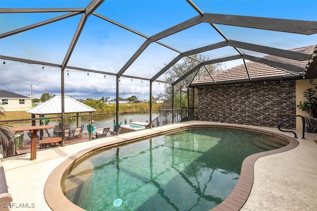 pool with glass enclosure, a patio area, and a water view