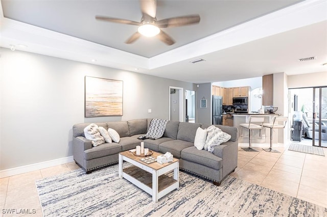 living room with a tray ceiling, visible vents, a ceiling fan, light tile patterned flooring, and baseboards