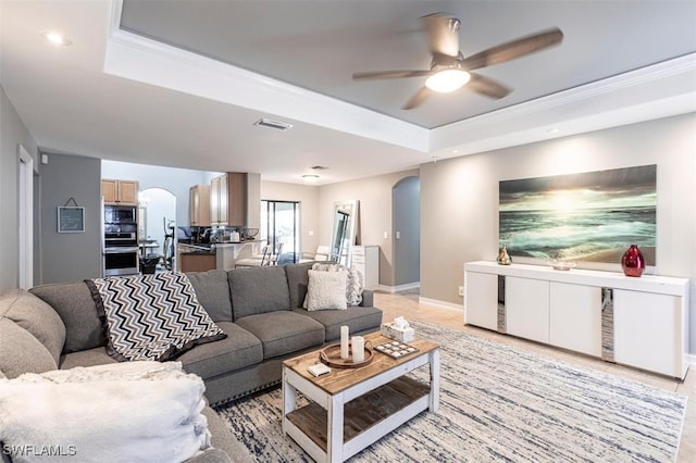 living room with arched walkways, ceiling fan, a tray ceiling, and visible vents