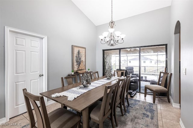 dining room featuring arched walkways, light tile patterned floors, an inviting chandelier, high vaulted ceiling, and baseboards