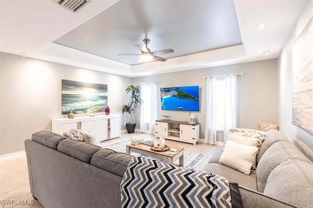 living room with light tile patterned floors, visible vents, a raised ceiling, baseboards, and ceiling fan