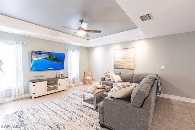 living room featuring a tray ceiling, light tile patterned floors, visible vents, ceiling fan, and plenty of natural light