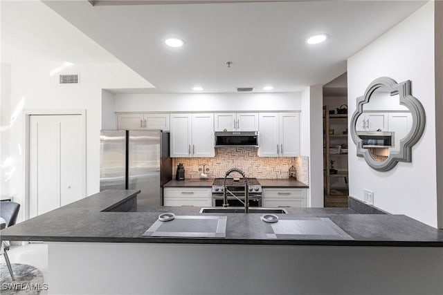 kitchen featuring stainless steel appliances, dark countertops, visible vents, backsplash, and white cabinets