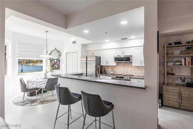 kitchen with stainless steel appliances, white cabinets, backsplash, dark countertops, and a kitchen bar