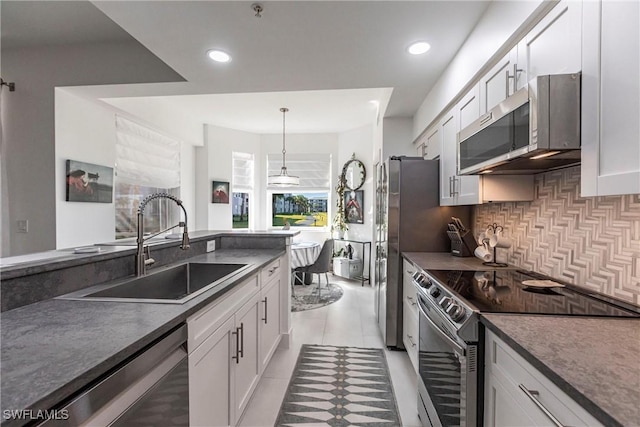 kitchen with tasteful backsplash, dark countertops, appliances with stainless steel finishes, white cabinetry, and a sink