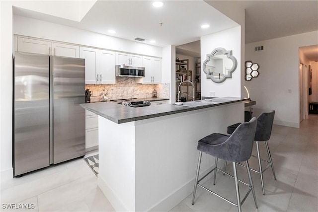 kitchen featuring a breakfast bar area, stainless steel appliances, dark countertops, backsplash, and a sink