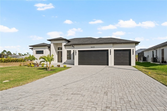 prairie-style house with decorative driveway, an attached garage, cooling unit, and a front yard