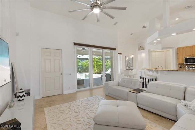 living room featuring baseboards, visible vents, ceiling fan, and a high ceiling