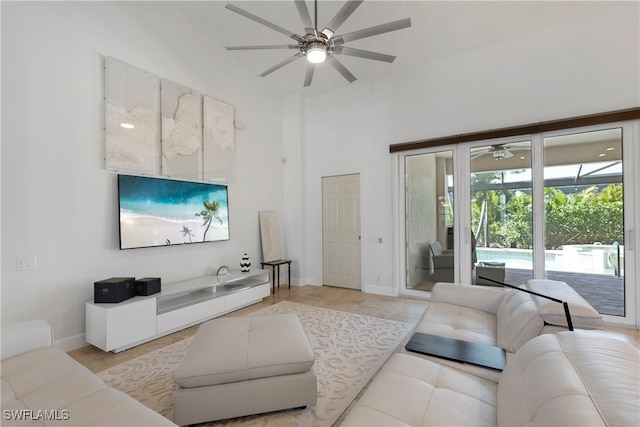 living room with a towering ceiling, ceiling fan, and baseboards