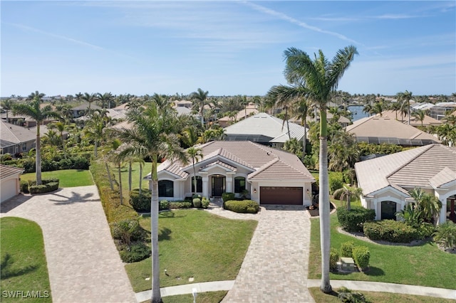 mediterranean / spanish-style house with a garage, a tile roof, decorative driveway, a residential view, and a front lawn