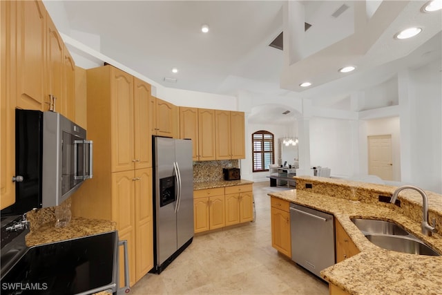 kitchen with arched walkways, light brown cabinetry, appliances with stainless steel finishes, and a sink