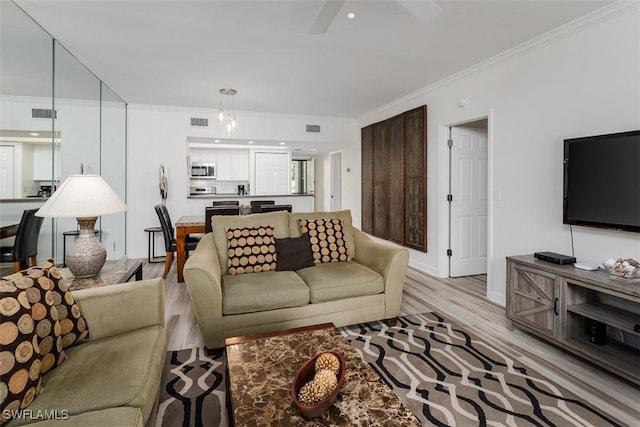 living area with ceiling fan, light wood-style floors, visible vents, and crown molding