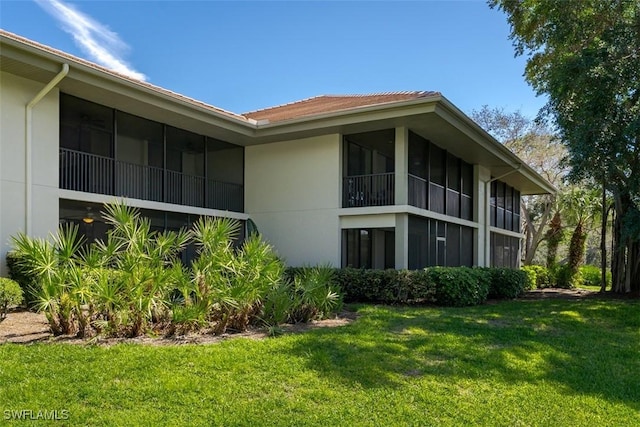 view of side of home with a sunroom, a yard, and stucco siding