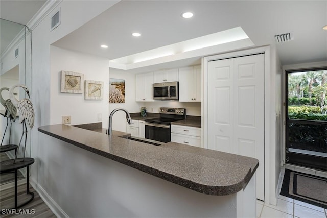 kitchen featuring stainless steel appliances, a peninsula, a sink, visible vents, and white cabinets