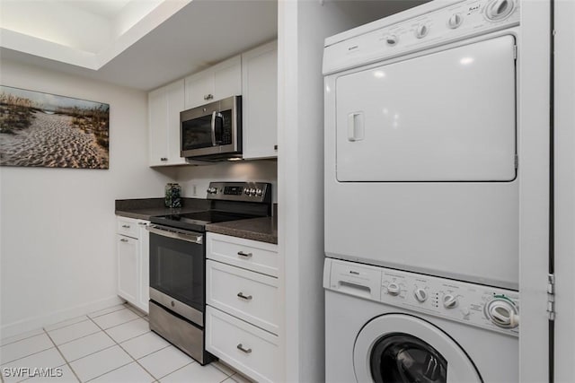 kitchen with white cabinets, dark countertops, appliances with stainless steel finishes, stacked washer / drying machine, and light tile patterned flooring