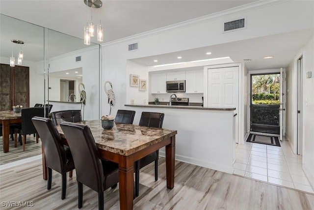 dining space with visible vents, crown molding, and light wood-style flooring