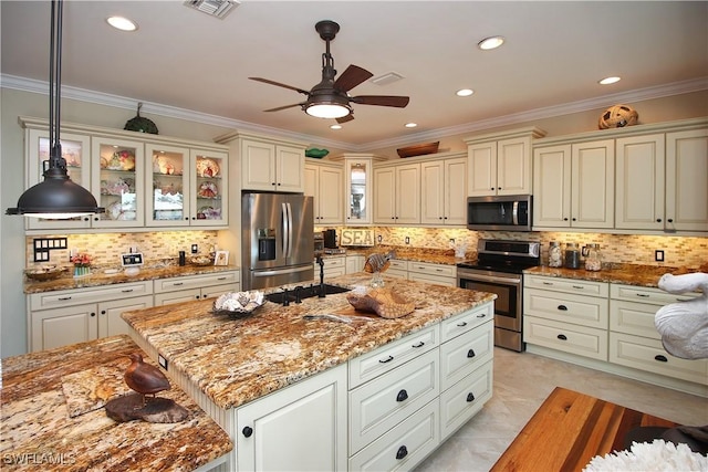 kitchen with visible vents, appliances with stainless steel finishes, ornamental molding, a kitchen island, and a sink