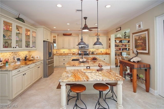 kitchen featuring a breakfast bar area, visible vents, ornamental molding, appliances with stainless steel finishes, and an island with sink