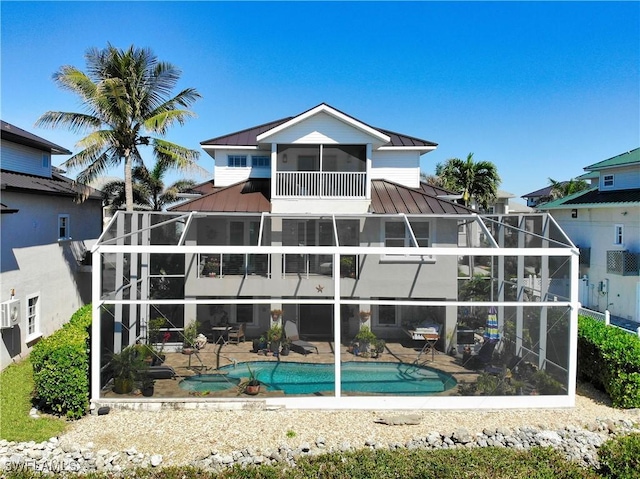 rear view of house with a balcony, glass enclosure, metal roof, a standing seam roof, and a patio area