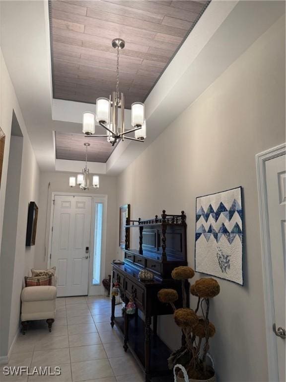 foyer with an inviting chandelier, a tray ceiling, and light tile patterned floors