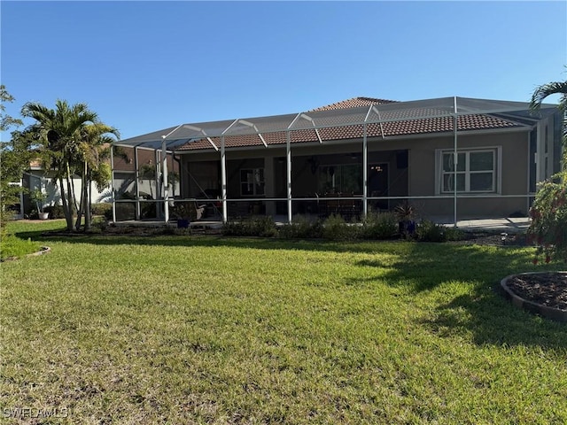 rear view of house with glass enclosure, a lawn, and a tile roof